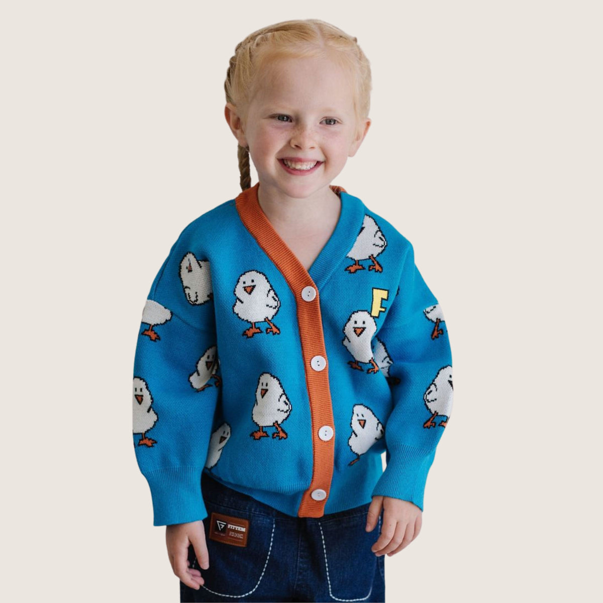 A smiling child wearing the blue Chicklet Cardi with orange trim and white chick motifs.